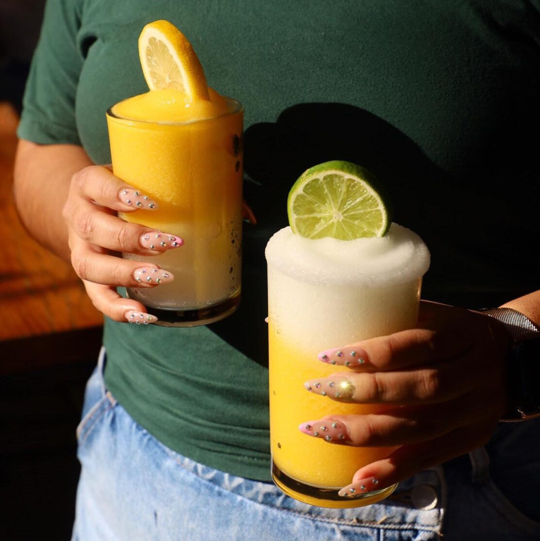 A woman holding a boozy slushee topped with a citrus garnish in each hand.