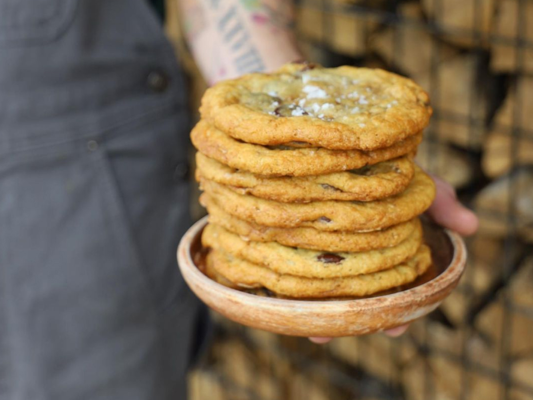 A person holding a wooden bowl filled with chocolate chip cookies.