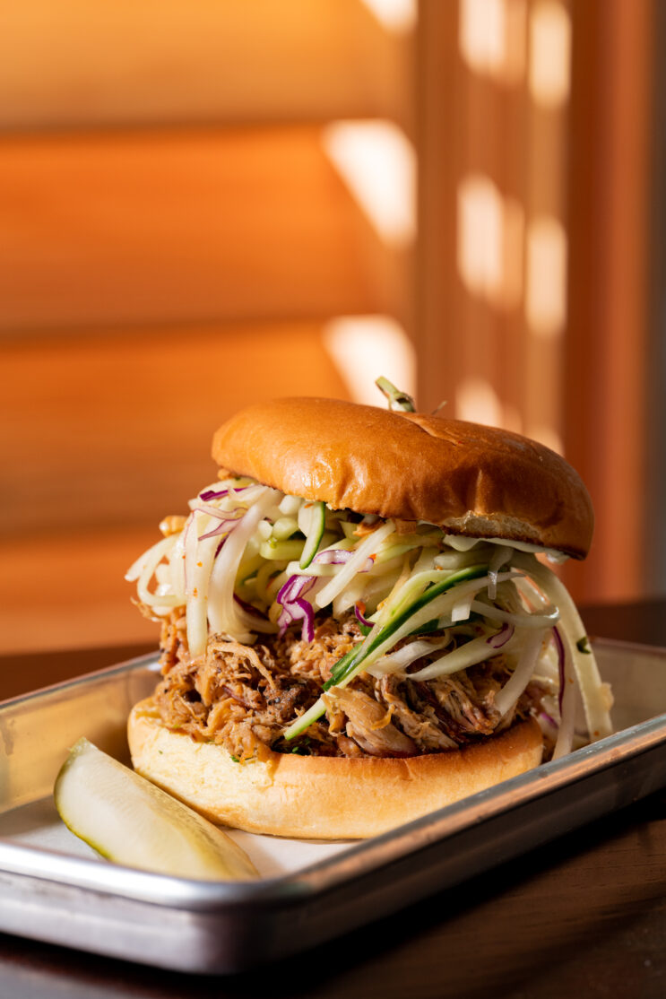 A close-up of a pulled pork sandwich served on a metal tray.
