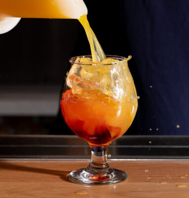 A person pouring a typhoon cocktail into a glass.