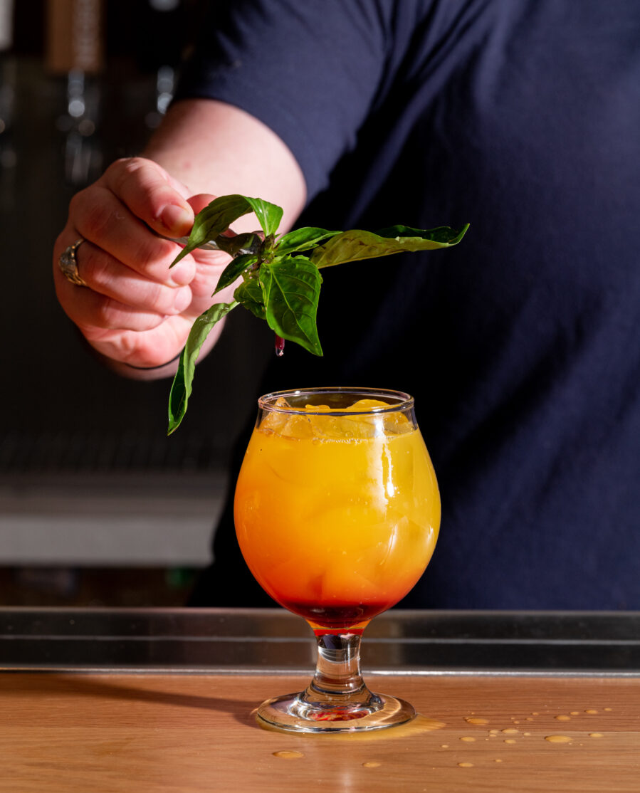 A person garnishing a typhoon cocktail in a glass with thai basil.