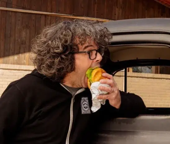 Aaron Franklin leaning on a truck and eating a hamburger.
