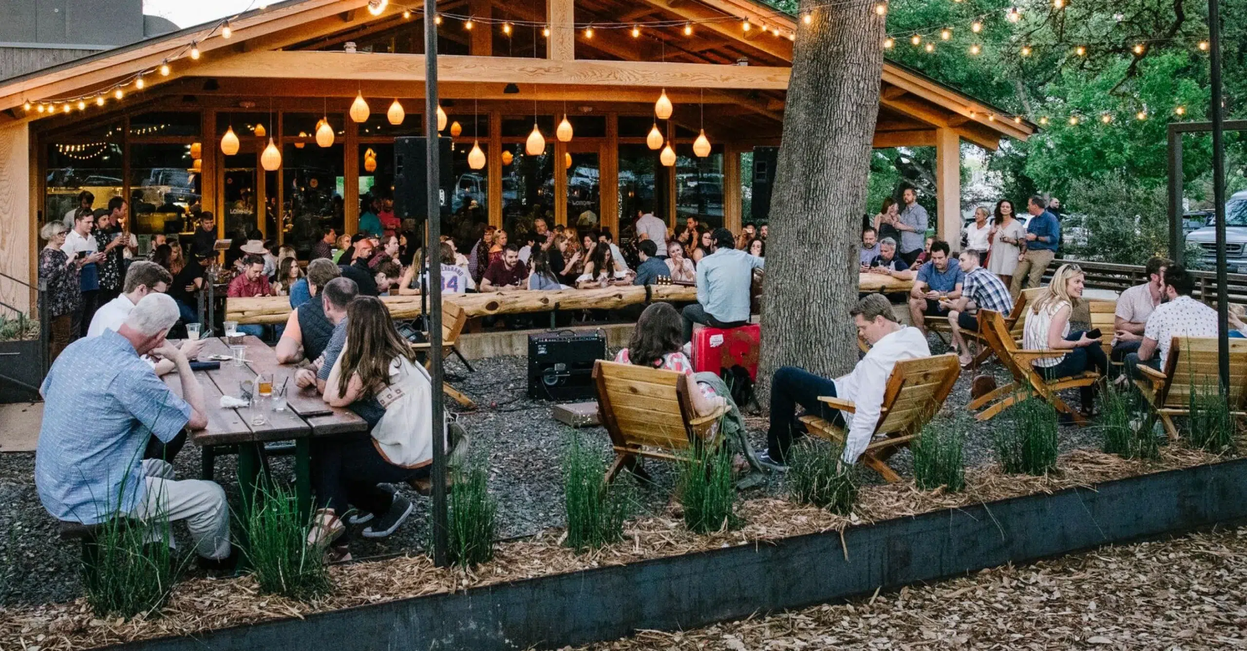 Groups of people sitting around wooden tables and in wooden chairs on the Loro Austin patio.