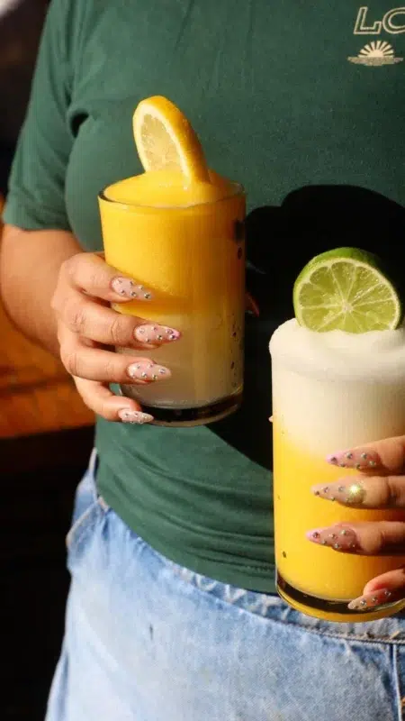 A woman holding a boozy slushee topped with a citrus garnish in each hand.
