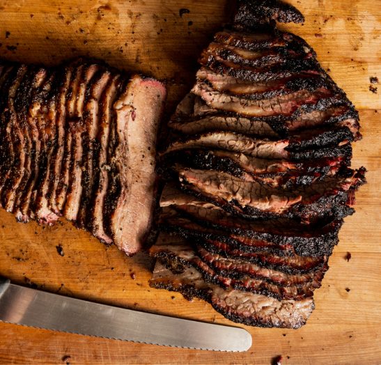 Slices of beef brisket resting next to a knife on a cutting board.