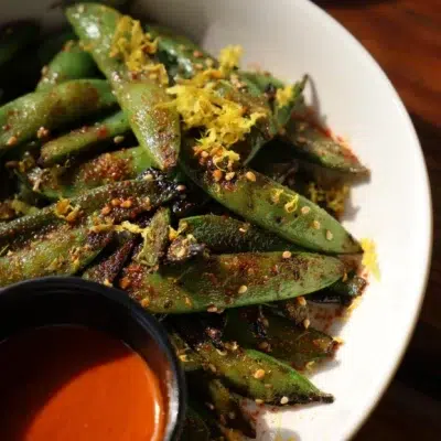 A white plate topped with oak grilled snap peas.