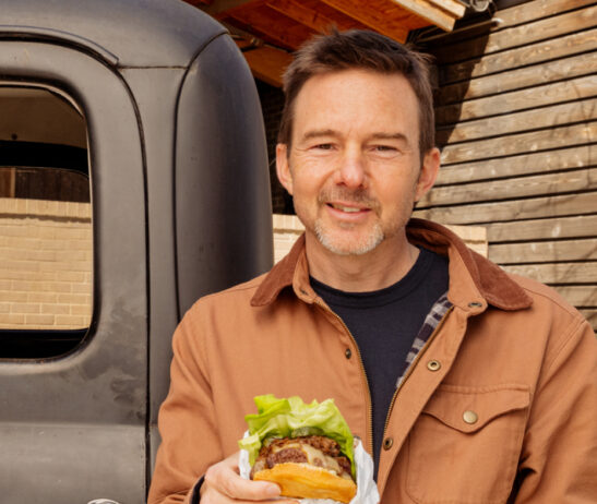 Tyson Cole holding a hamburger in front of a truck.