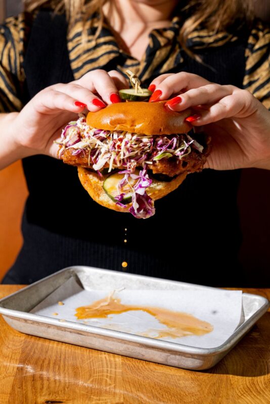 A woman in a black shirt holding a crispy smoked chicken sandwich.