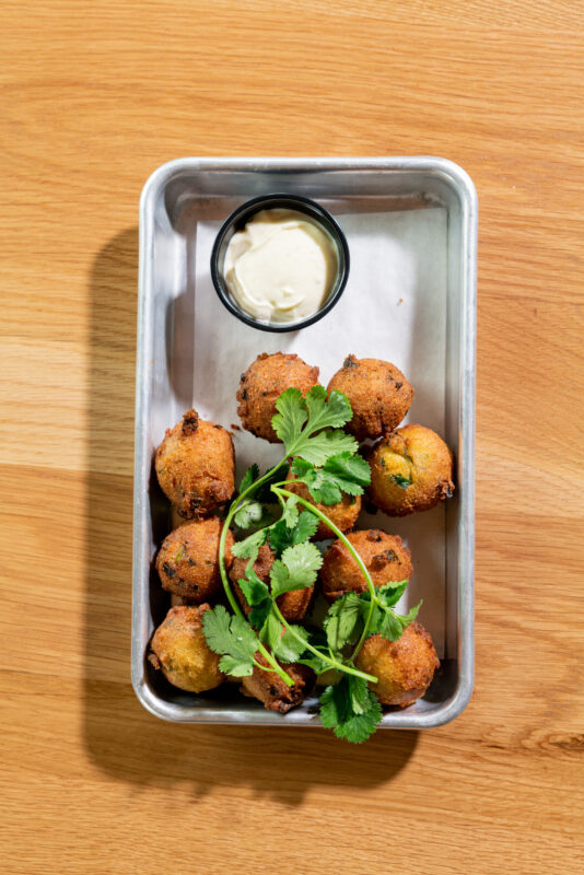 A close-up of green curry hushpuppies served on a metal tray.