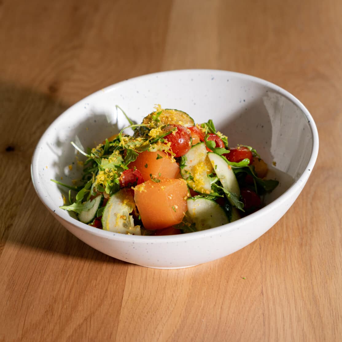 A white bowl filled with a salad on top of a wooden table.
