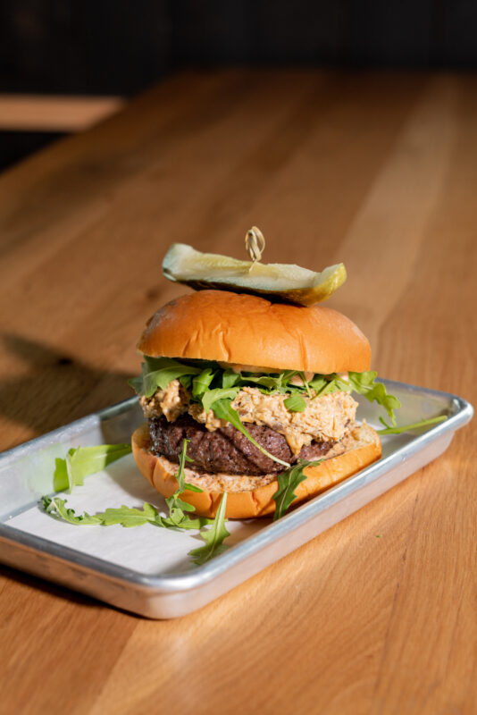 A close-up of a caramelized onion-cheddar burger served on a metal tray.