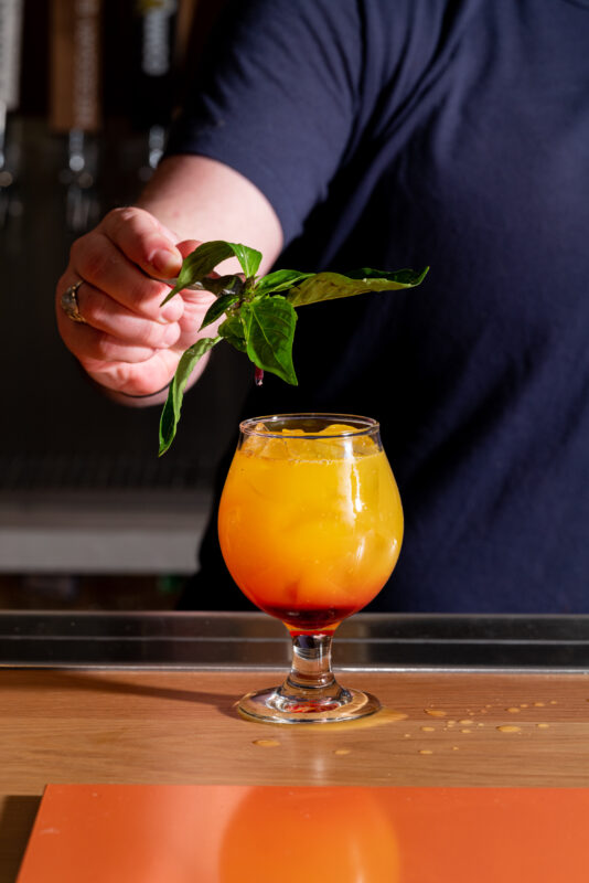 A person garnishing a typhoon cocktail in a glass with thai basil.