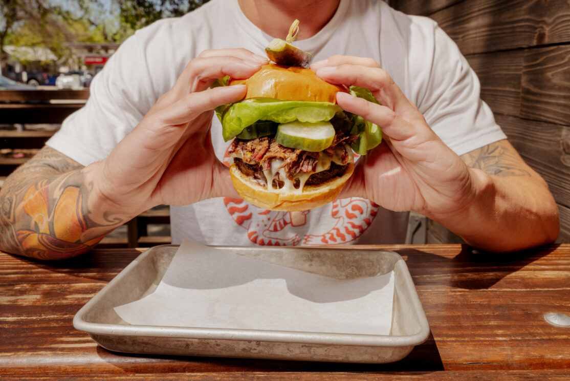 A man sitting at a table with a Loro cheeseburger in front of him.