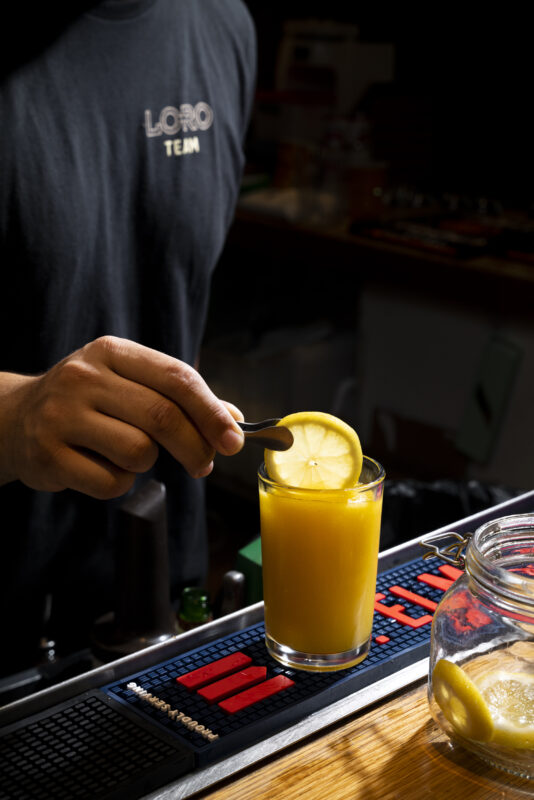 A person garnishing a boozy slushee in glass with a slice of lemon.