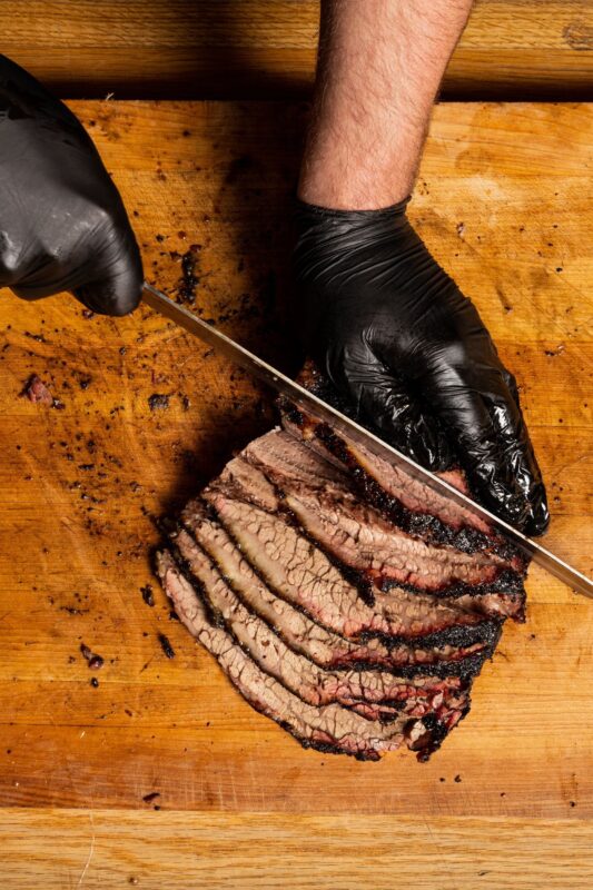 A chef cutting beef brisket with a knife on a cutting board.