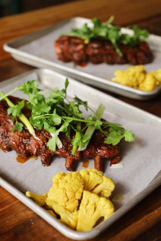 A close-up of baby back pork duroc ribs served on a metal tray.