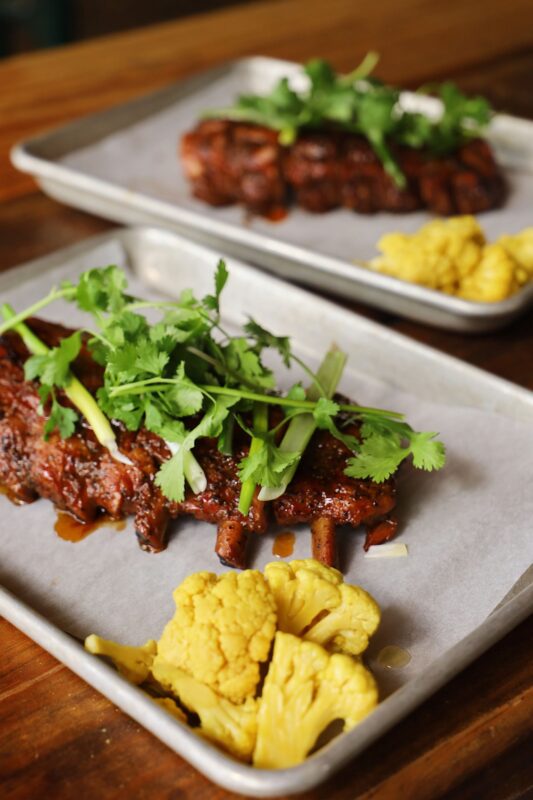 A close-up of baby back pork duroc ribs served on a metal tray.