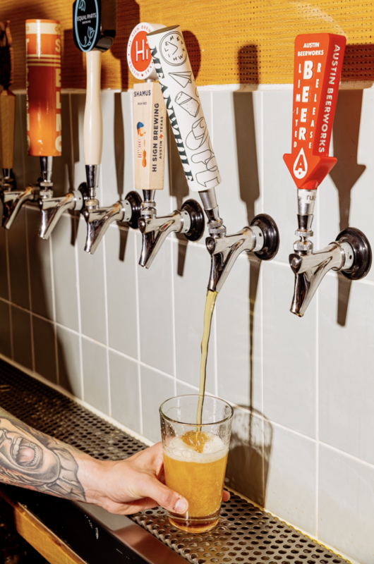 A person pouring a beer from a tap into a pint glass.