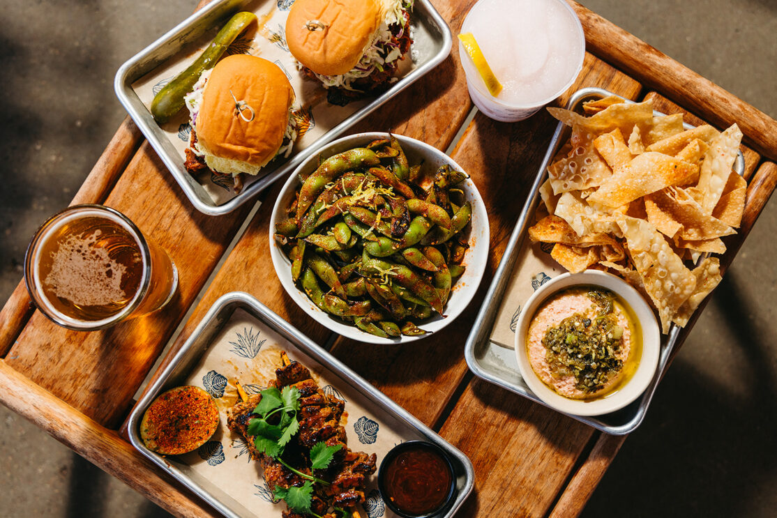 happy hour spread including queso and chips, pork skewer, edamame and pork sliders