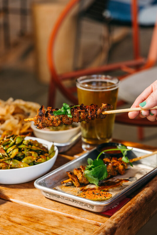 hand holding pork skewer in front of happy hour spread