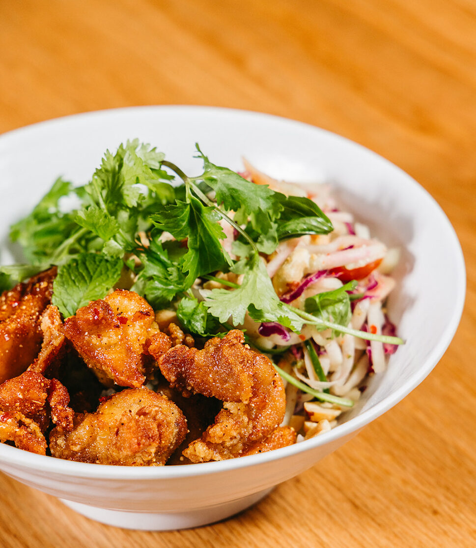 white bowl with rice, crispy friend chicken, herbs and papaya salad