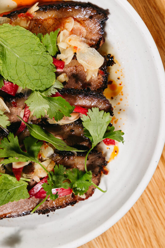 close up of smoked beef brisket topped with thai herbs