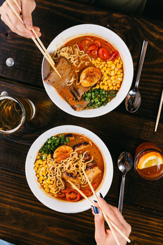 top down view of 2 bowls of spicy Japanese curry ramen with a glass of beer