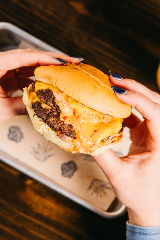 hands holding double smash burger with yuzu 1000 island sauce and American cheese
