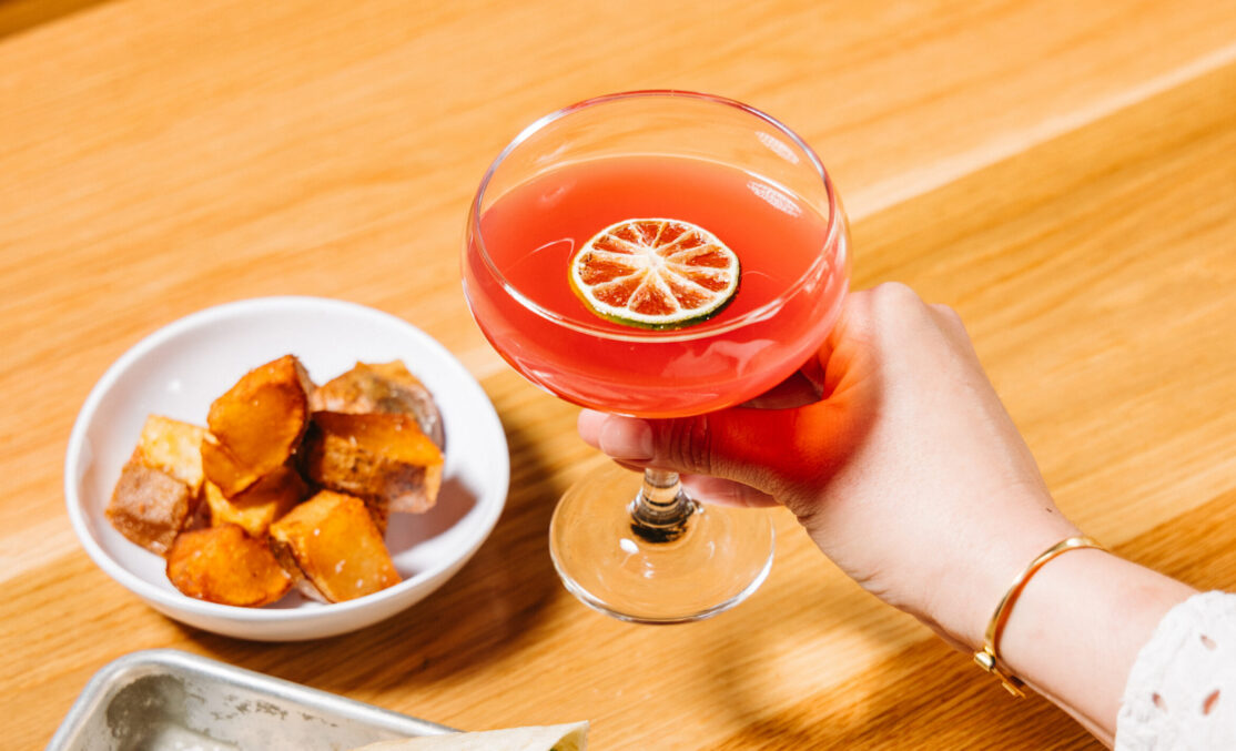 hand holding red cocktail in coupe glass