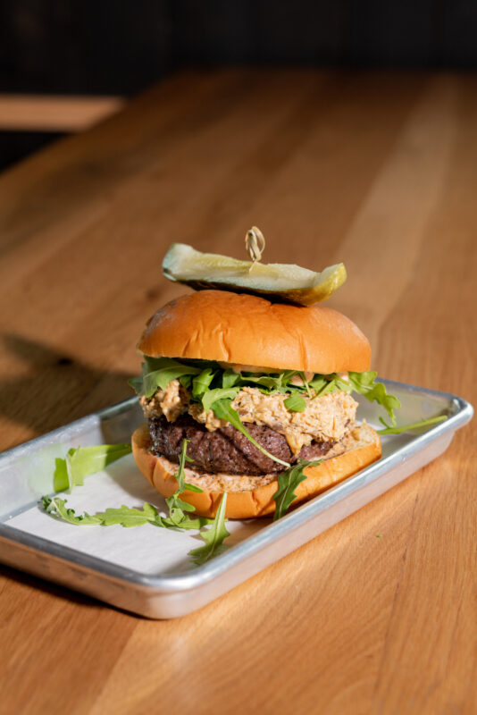 thick burger with pimento cheese and pickle on a wooden table
